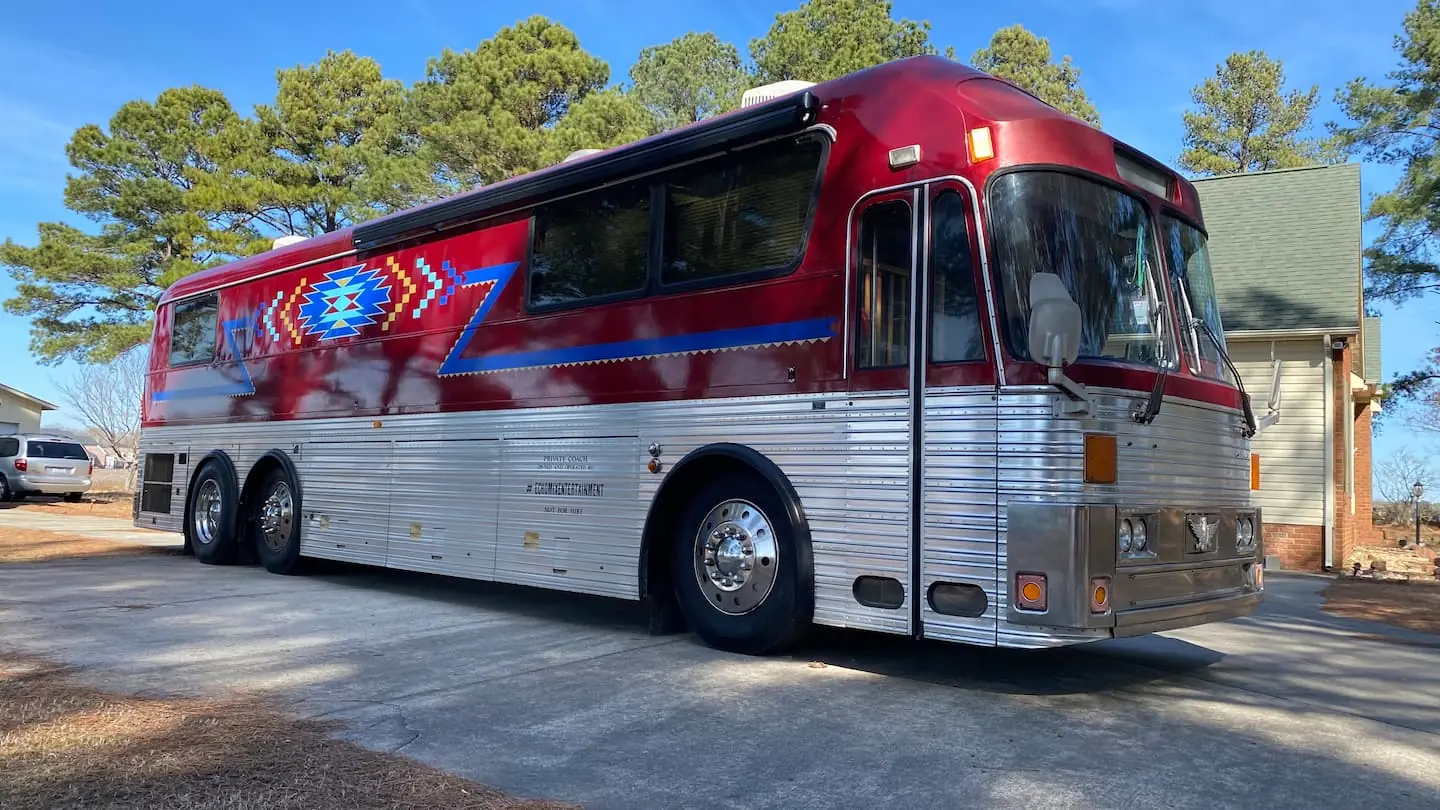 Original Airbnb daylight photograph of the red and silver vintage Eagle tour bus with blue geometric side artwork parked on pavement